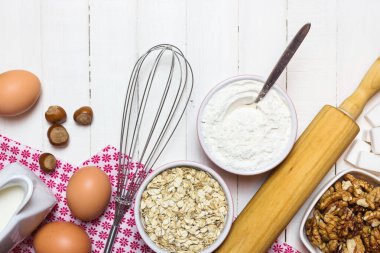 Kek pişirmek için malzemeler ve aletler. Beyaz ahşap masada yumurta, un, süt, şeker, fındık ve çikolata. Pişirme veya pişirme konsepti.