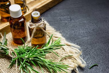 Biberiye bitkisi dalları ve siyah taş arka planda biberiye yağı şişeleri. Bitkisel aromaterapi kavramı.