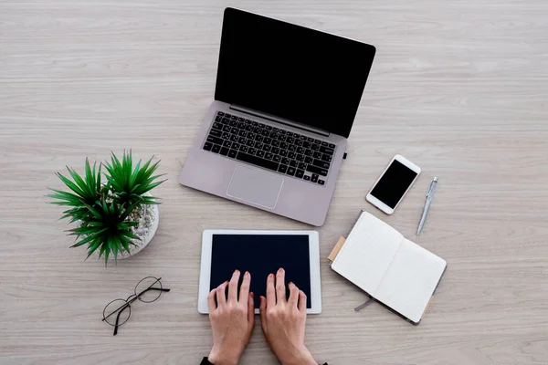 Kadın, laboratuvar, tablet ve akıllı telefon gibi çeşitli ofis aletleriyle çalışıyor. Ofisteki ahşap masanın üzerindeki küçük deftere yazıyor..