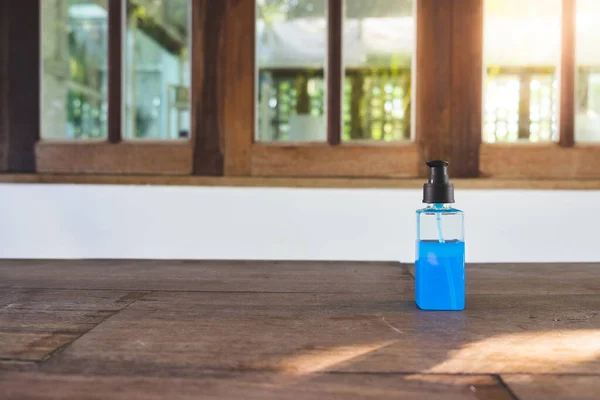 Blue Ethyl alcohol gel or hand sanitizer for coronavirus (COVID-19) protection. in the plastic bottle on the wooden desk in front of the windows with flare light
