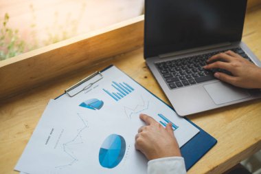İş adamı, ahşap masadaki iş verilerini analiz etmek için dizüstü bilgisayarının klavyesini yazarken iş veri tablosunu işaret ediyor. Mali ve İş Konsepti.