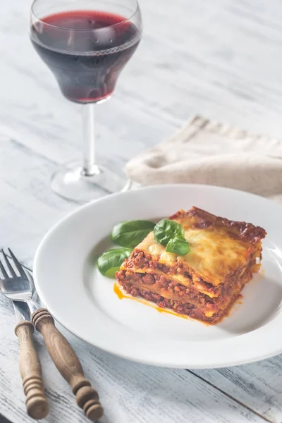Portion of lasagne with a glass of wine on the wooden table — Stock Photo, Image