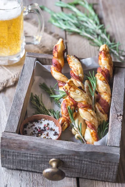 Bâtonnets de pain enveloppés de bacon avec tasse de bière — Photo