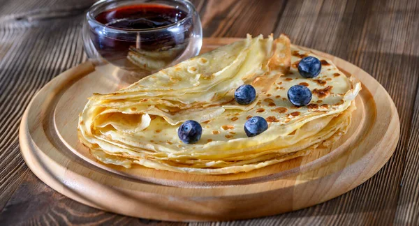 Crepes with fresh blueberries and berry syrup on wooden board