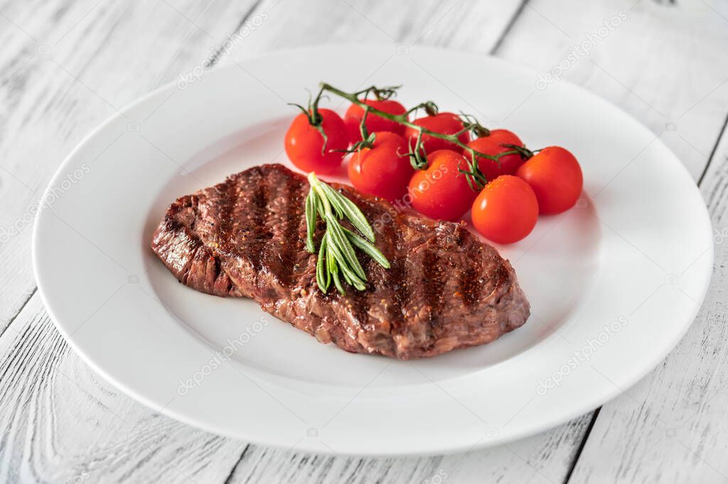Beef steak with cherry tomatoes and fresh rosemary on white plate