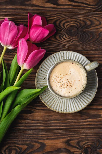 pink tulips, cup with coffee on a wooden background, copy space