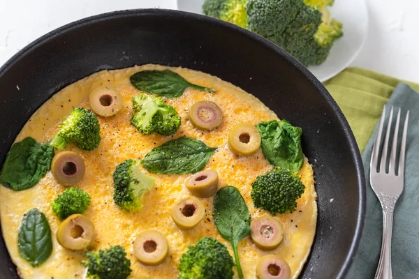 Омлет с брокколи, шпинатом и оливками на сковороде. Фриттата - итальянский омлет с зелеными овощами . — стоковое фото