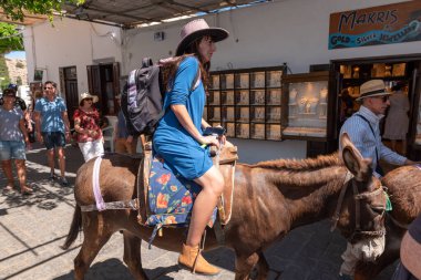 Rhodes, Greece - May 14, 2018: Woman riding donkey. Using donkey taxi to the Acropolis is a popular tourist attraction in Lindos.