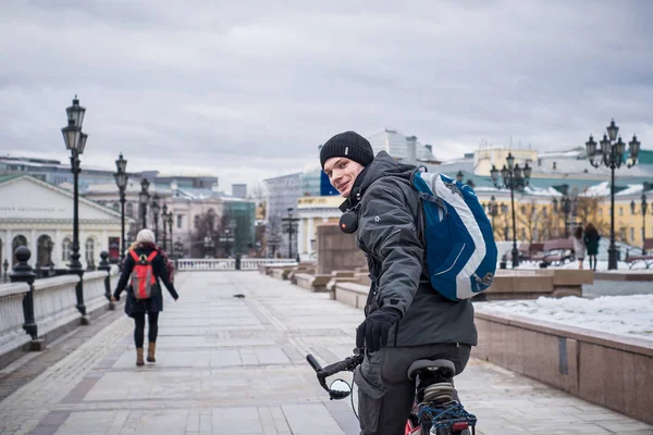 A young man in a warm jacket and hat on a bicycle in the center of Moscow in the winter — Stock Photo, Image