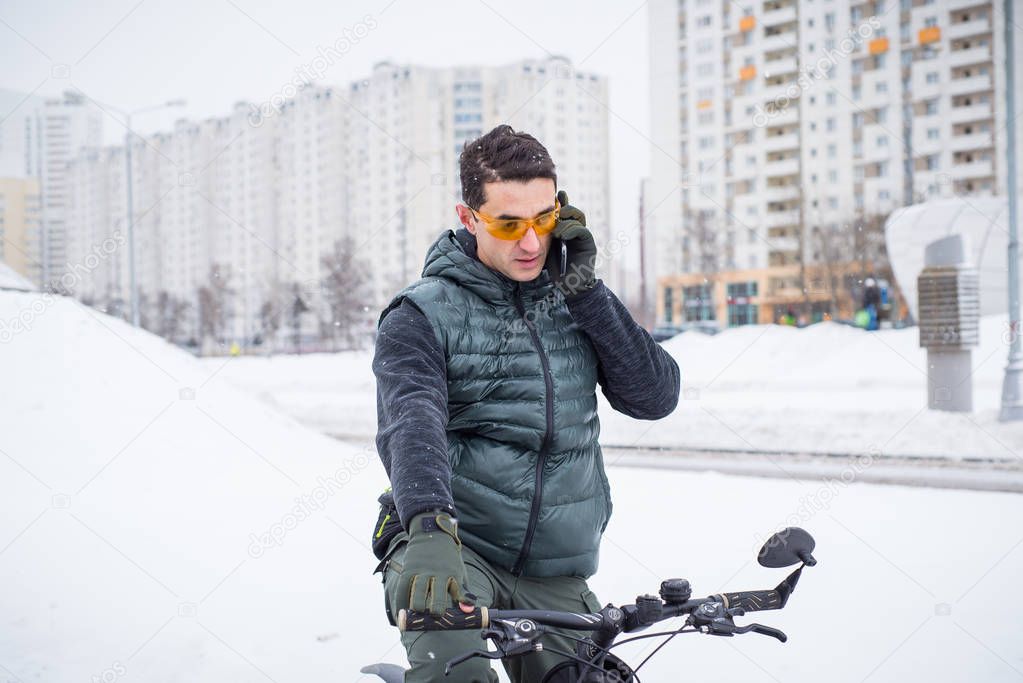 Young man on a bicycle in the winter in the city is on the phone