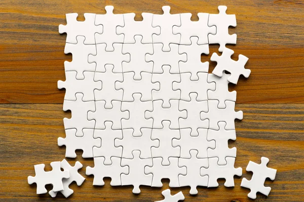 Weiße Puzzleteile auf Holz-Hintergrund. — Stockfoto