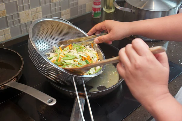 Hand mixing vegetables in steel strainer