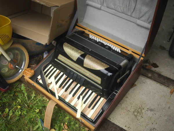 Discarded household objects with broken harmonica in a case
