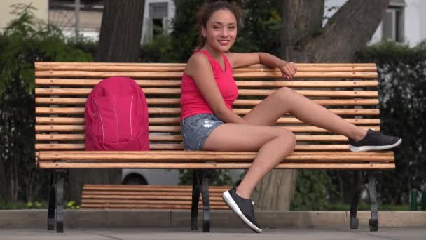 Латиноамериканка-студентка, сидящая на скамейке в парке — стоковое видео