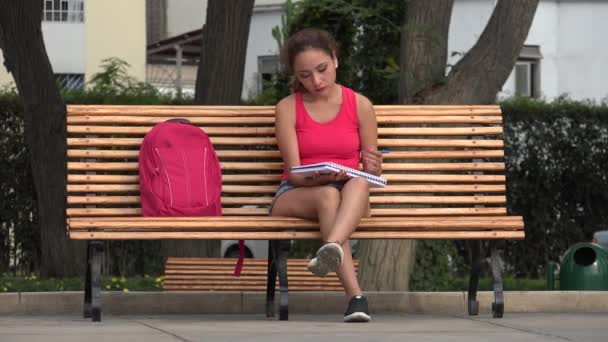 Studentin sitzt auf Parkbank und zeichnet in Notizbuch — Stockvideo