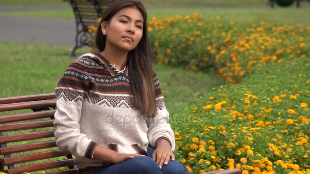 Испанская женщина-подросток, сидящая одна на скамейке запасных в парке — стоковое видео