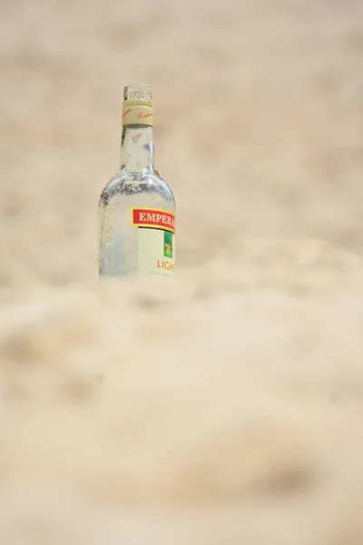 Botella de vidrio de alcohol en la arena de la playa —  Fotos de Stock