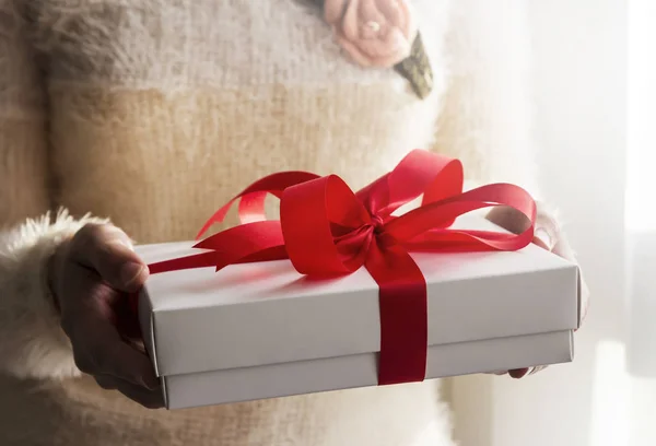 Joven mujer manos sosteniendo caja de regalo blanca con cinta roja — Foto de Stock