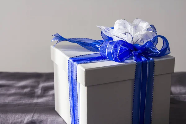 Ezüst ajándék doboz, kék-fehér szalaggal az ágyon — Stock Fotó