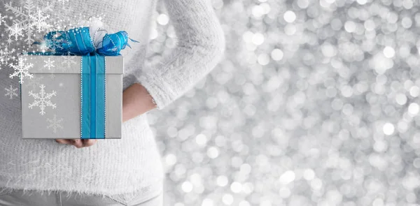 Молодая женщина прячет серебряную подарочную коробку за спиной — стоковое фото