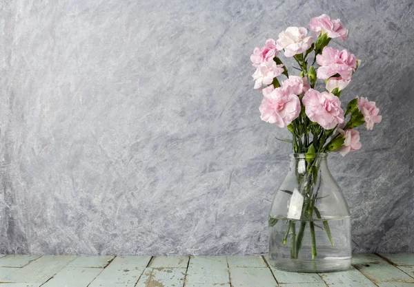 Pink carnation flowers in clear bottle on old wood — Stock Photo, Image