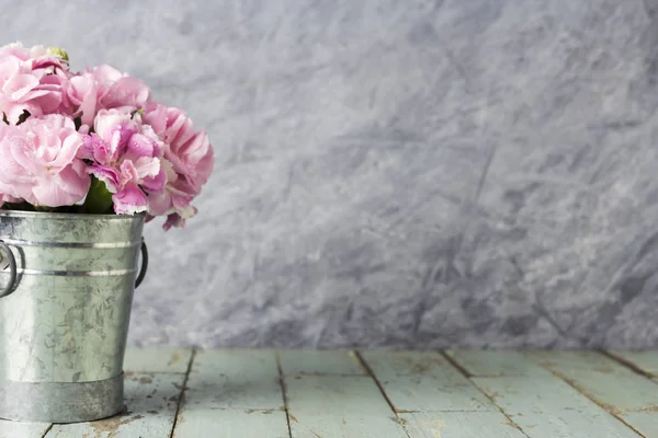 Ροζ γαρύφαλλο λουλούδια σε κουβά με ψευδάργυρο σε παλιό ξύλο — Φωτογραφία Αρχείου