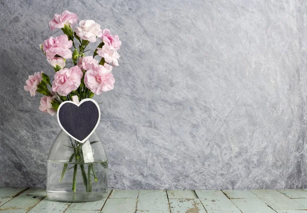 Flores de clavel rosa en botella transparente con madera de corazón —  Fotos de Stock