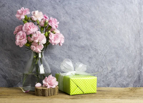 Pink carnation flowers in bottle and green gift box on old wood Royalty Free Stock Photos
