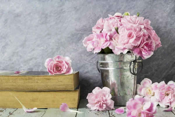 Flores de cravo rosa em balde de zinco e livro velho sobre madeira de mesa — Fotografia de Stock