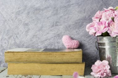 Pembe yün kalp üzerinde eski kitap ve karanfil çiçek örgü