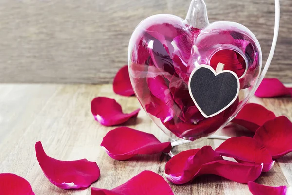 Pétalos de rosa roja en jarrón de corazón sobre fondo de madera — Foto de Stock