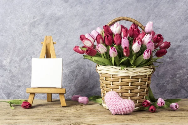Conceitos de amor de flores de tulipa em cesta de madeira com coração rosa e quadro de lona em branco na pintura cavalete para dia dos namorados e casamento — Fotografia de Stock