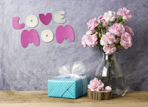 Mothers day concept of love mom letter pink carnation flowers in bottle and blue gift box on old wood — Stock Photo, Image