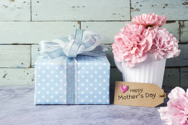 Wiadomość dzień matki Happy na brązowy papier tag i różowy Goździk kwiat w białym polu Puchar i prezent — Zdjęcie stockowe
