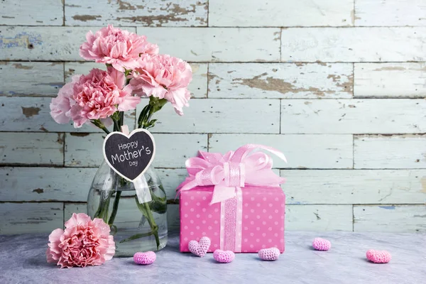 Joyeux message de la fête des mères sur le bois de coeur et la fleur d'oeillet rose en bouteille claire et boîte cadeau — Photo