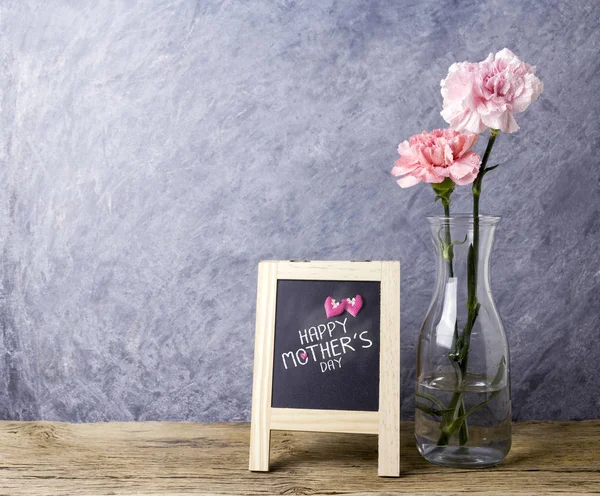 Joyeux message de la fête des mères sur tableau et fleur d'oeillet rose en bouteille transparente sur vieux bois avec espace de copie — Photo