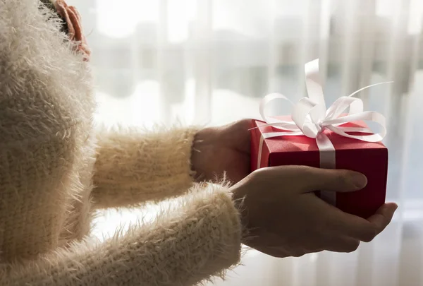Młoda kobieta ręce, trzymając czerwone pudełko z białą tasiemką na Boże Narodzenie i nowy rok i inne uroczystości — Zdjęcie stockowe