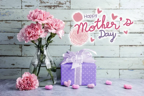 Feliz mensaje del día de las madres sobre fondo de madera y flor de clavel rosa en botella clara y caja de regalo — Foto de Stock