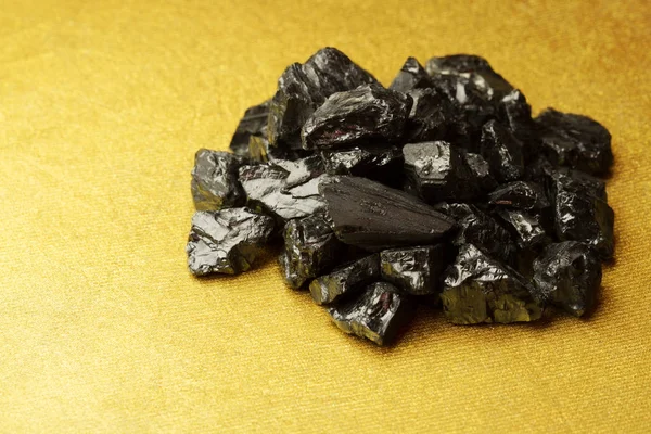 Bryłki węgla surowego na złotym tle teksturowane — Zdjęcie stockowe