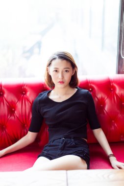 Seksi kadın kırmızı deri koltukta oturuyor, kameraya bakıyor..