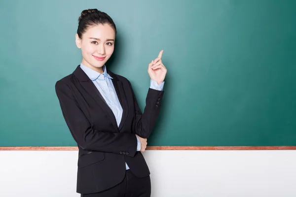 portrait of female teacher pointing to chalkboard.