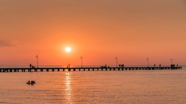 Deniz yürüyüş insanlar siluetleri ile eski İskelesi, gün batımından önce bir