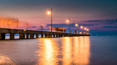 Deniz yürüyüş insanlar siluetleri ile eski İskelesi, güneş battıktan sonra bir