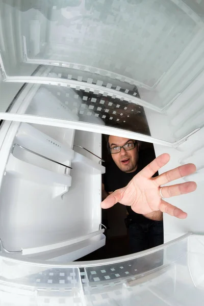 Funny scene of hungry young man opening the door of the fridge