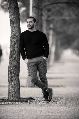 Emin sert yakışıklı adam karşı bir ağaca yaslanmış poz,