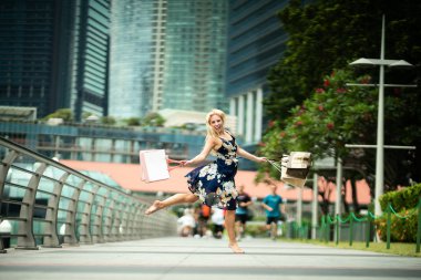 Alışveriş sevinç... Heyecanlı güzel çiçekler, gökdelenler ile sokaklarda alışveriş torbaları ile gündelik mavi elbise giyen kadın üzerinde air, 