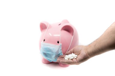 Ameliyat maskesi takan ve el ele tutuşan bir kumbara. Dünya ekonomisinde pandeminin etkisi.