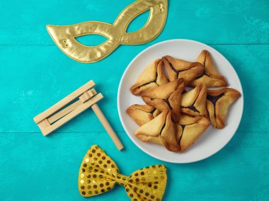Hamantaschen tanımlama bilgileri maske ve gürültü maker ile beyaz masada. Purim tatil kutlaması. Üstten Görünüm