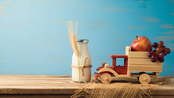 Milk bottle and toy truck with fruits on wooden table. Jewish holiday shavuot concept.