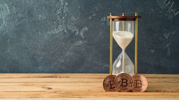 Bitcoins and hourglass on wooden table — Stock Photo, Image